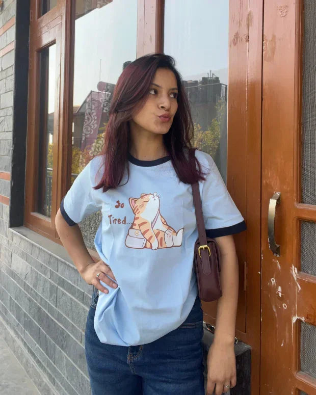 Tired Tap Out T-Shirt - light blue regular tee with black trim, featuring a lounging cartoon cat graphic, worn by model.