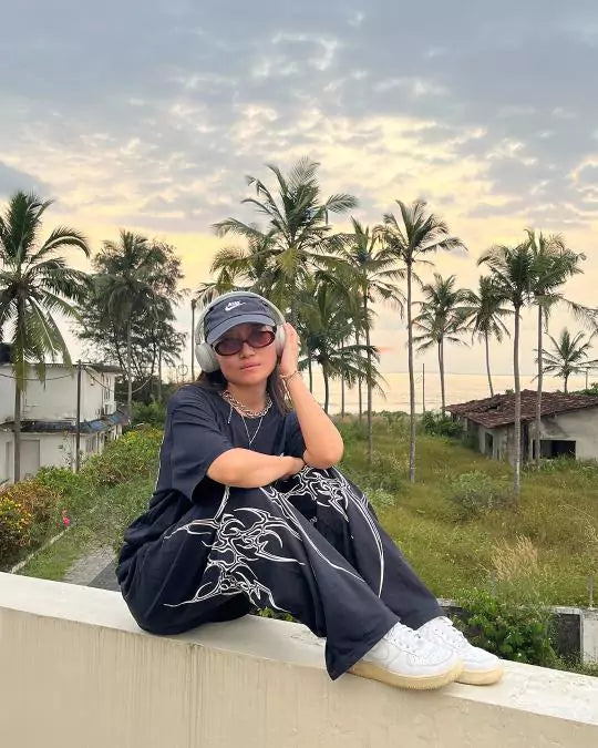 Arlo Black Gangster Oversized T-shirt โ black tee with white graphic print, worn by model outdoors among palm trees.