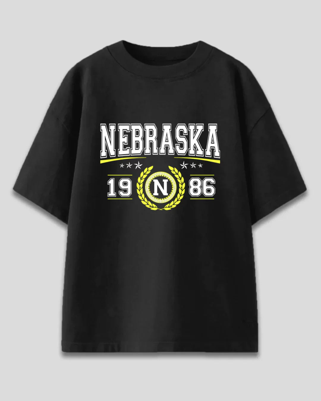 Arlo Nebraska Oversized T-Shirt – black cotton graphic tee with Nebraska 1986 crest in white and yellow, flat lay