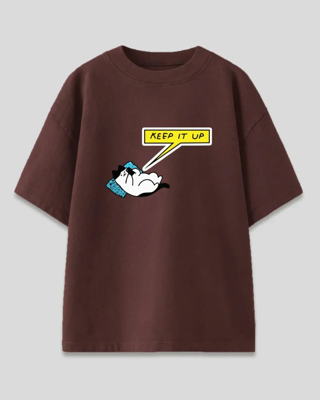 Keep It Up Oversized T-Shirt – brown DKY graphic tee with a white cat on a blue pillow and a yellow speech bubble.