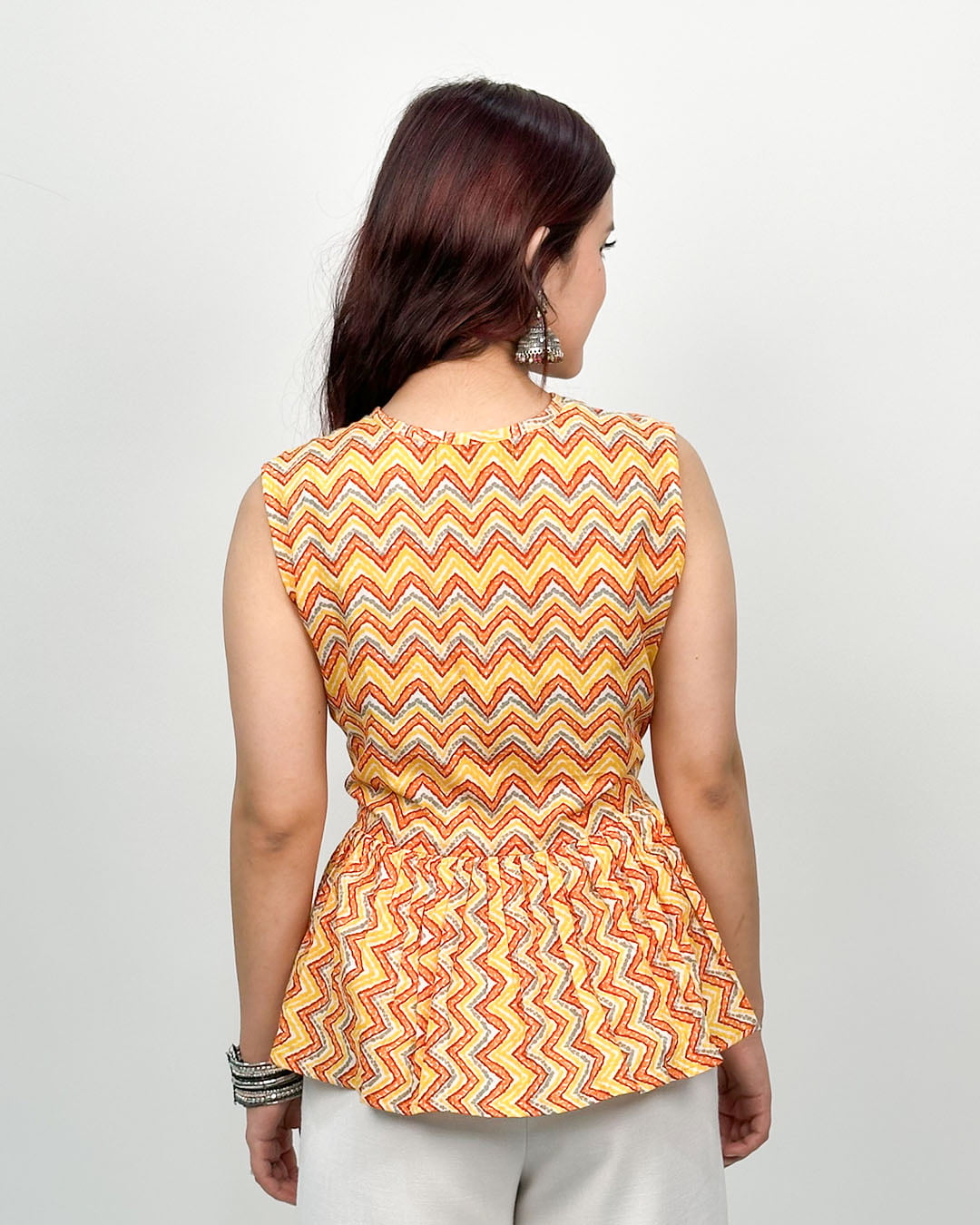 Tangerine Peplum Cotton Top ā orange-yellow zigzag print sleeveless peplum top, worn by model.