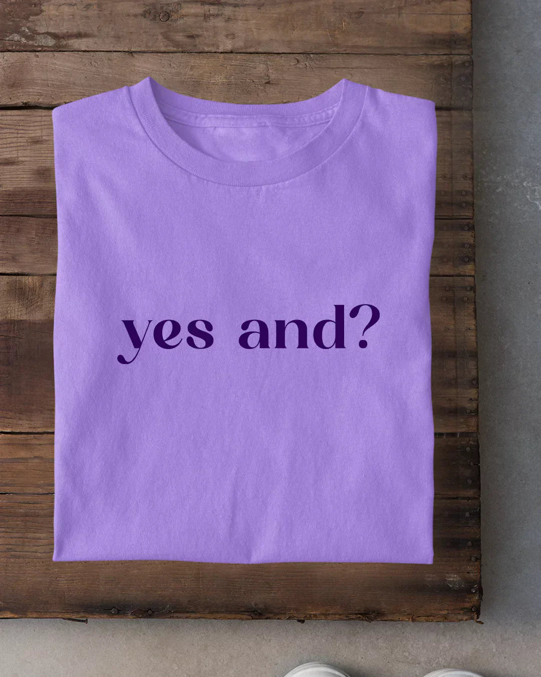 Yes And T-Shirt โ lilac regular tee with yes and? print, folded on a wooden surface