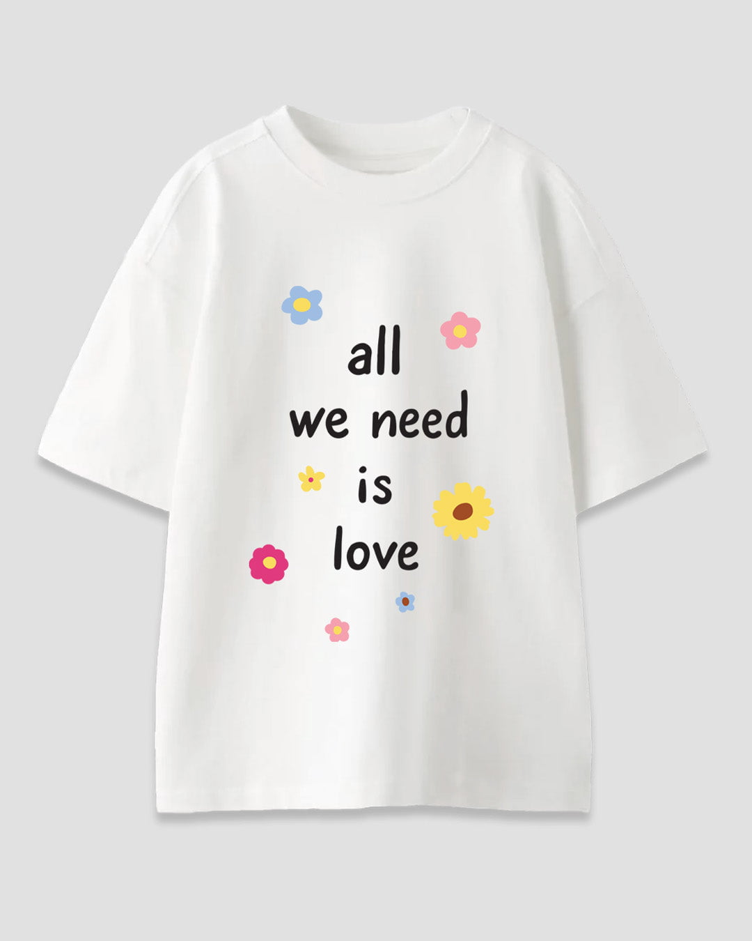All We Need Is Love Oversized T-Shirt – white oversized graphic tee with colorful flowers and the phrase all we need is love, shown in flat lay