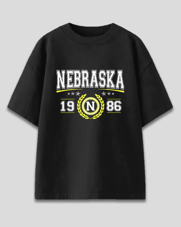 Arlo Nebraska Oversized T-Shirt – black cotton graphic tee with Nebraska 1986 crest in white and yellow, flat lay