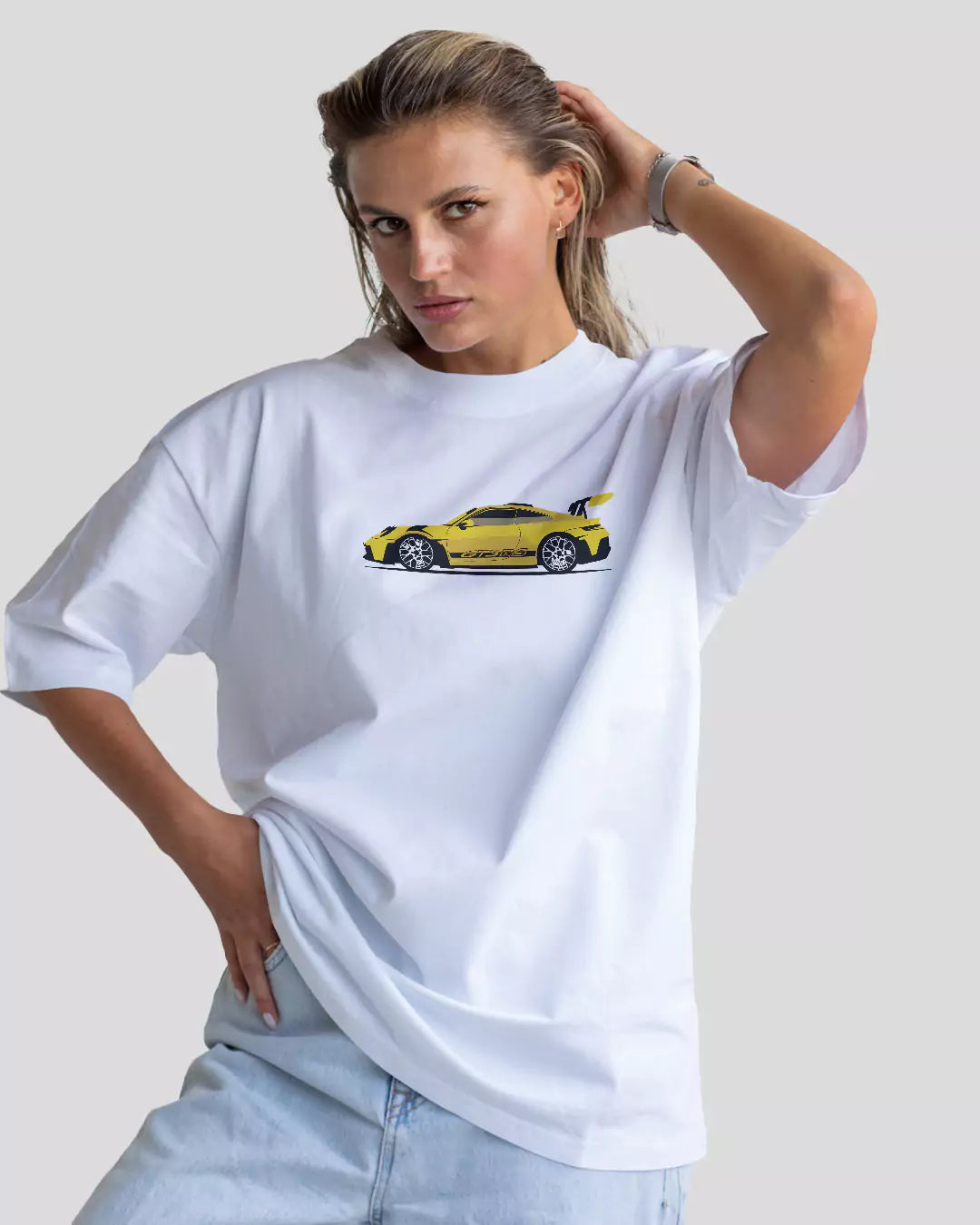 Arlo Need Money For Porsche Oversized T-Shirt – white oversized graphic tee with a yellow car graphic, worn by model.