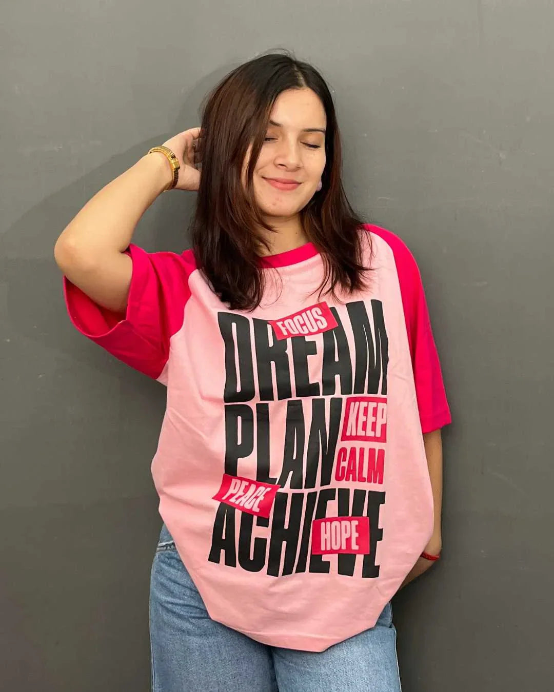 Dream Raglan Oversized T-Shirt in pink with magenta sleeves, bold black DREAM PLAN ACHIEVE graphic, worn by model
