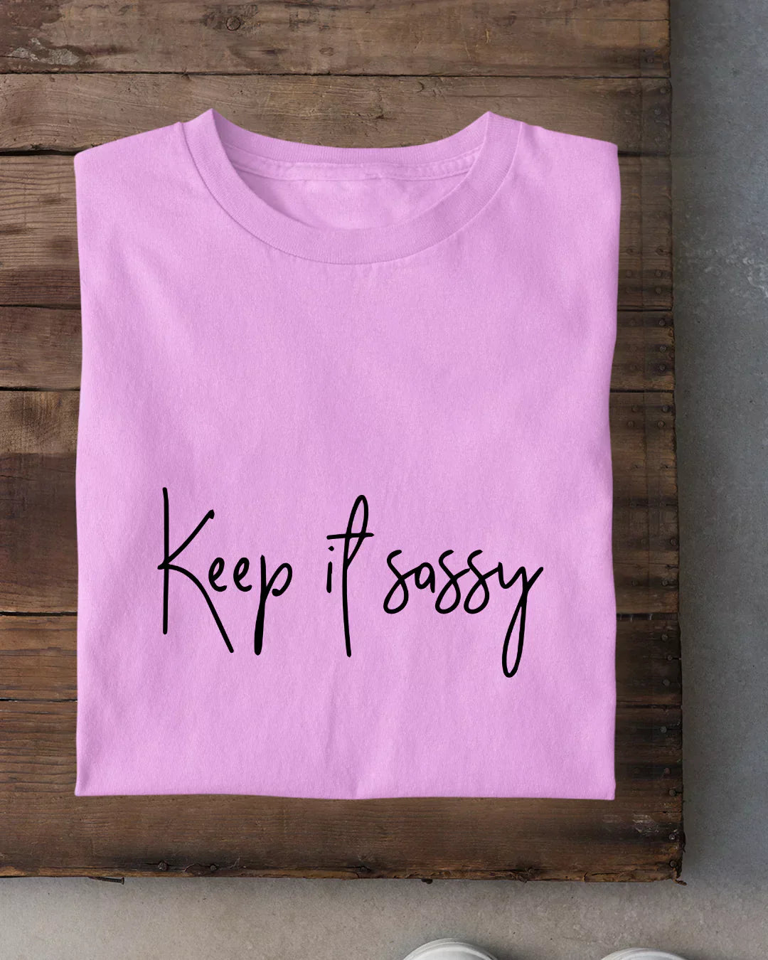 Lilac Keep It Sassy T-Shirt – regular tee with black script Keep It Sassy, laid flat on wood