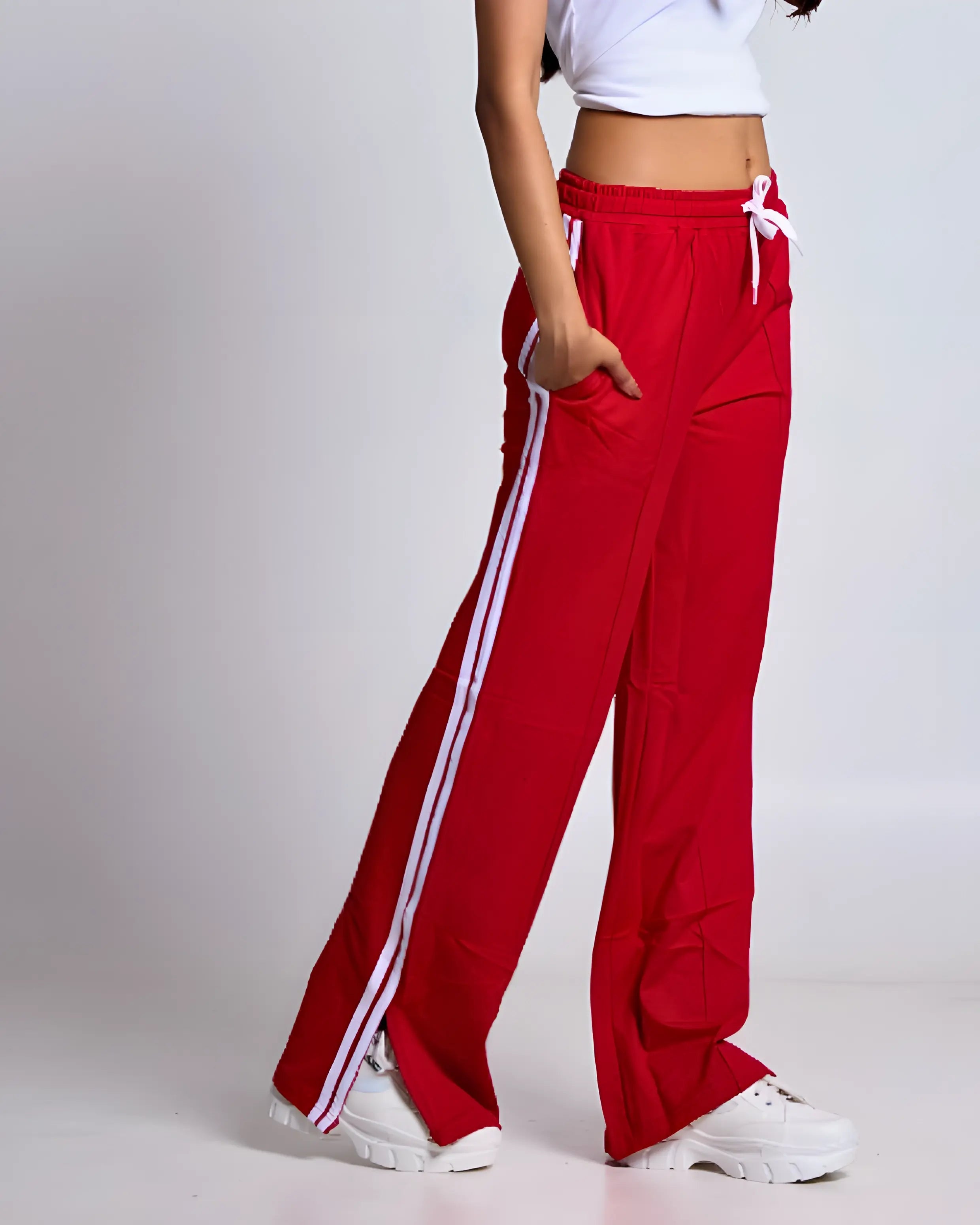Red Gossip Pants – red jogger pants with white side stripes and a drawstring waist, shown on a model in sneakers.